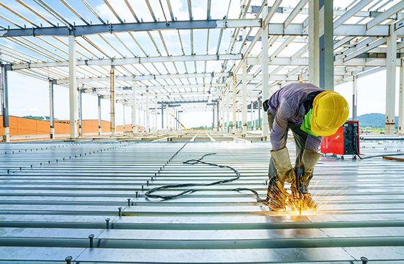 Construction worker welding on the middle level of a commercial building's floor.
