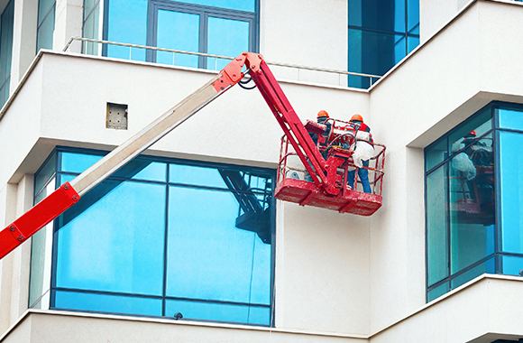 Two workers on a boom lift performing exterior finishing work on a building.